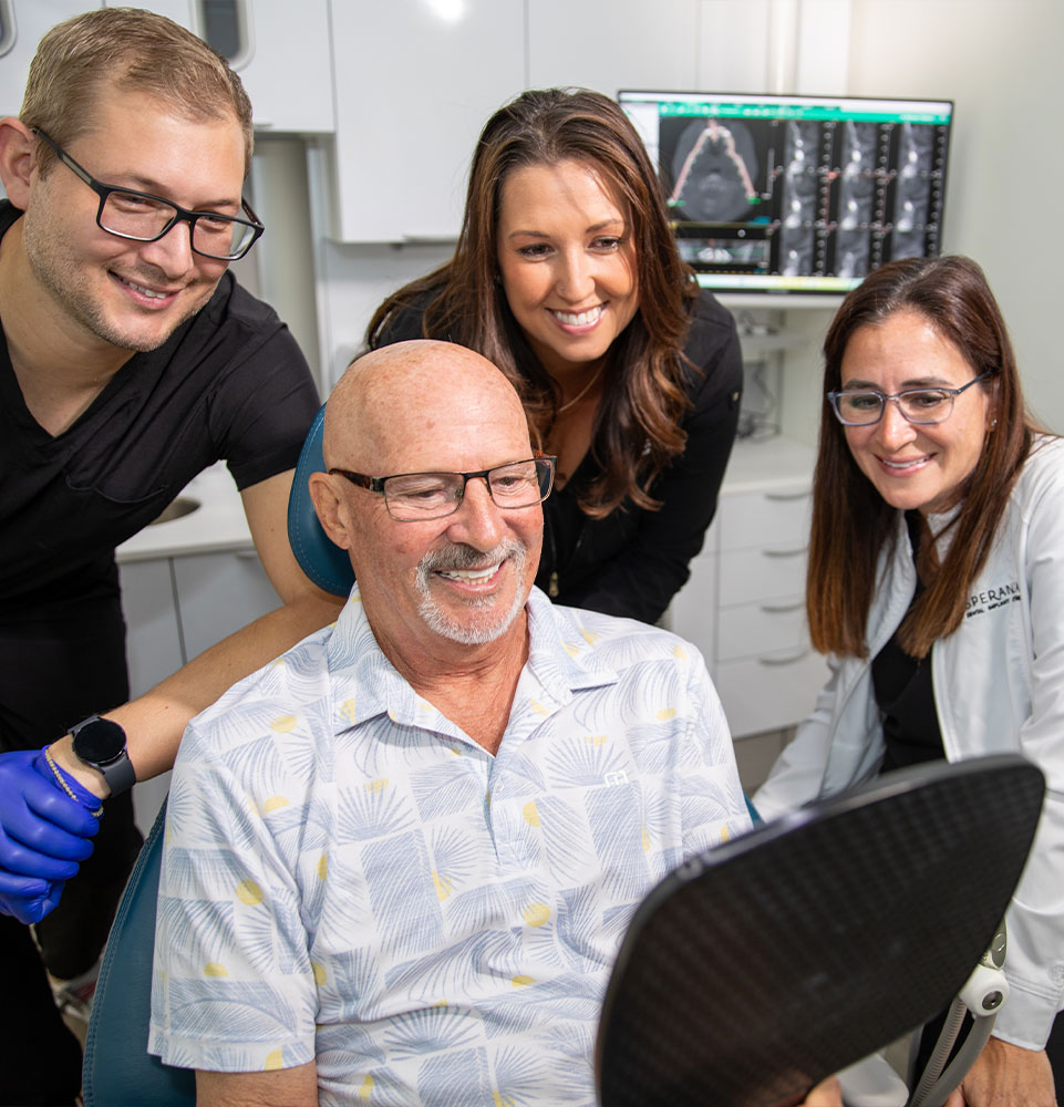 Patients and team members looking into mirror looking at patients new smile